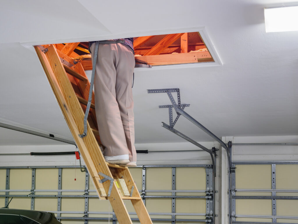 Man inspecting garage attic. Male homeowner climbing wooden pull